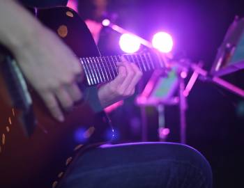 A person sits on a stool and plays their acoustic guitar on a dive bar stage