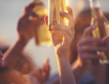 Hands raise beer bottles during a sunset show at a beach bar