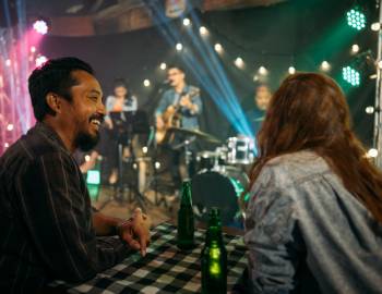 Two people enjoy company over beers in a dive bar while a live band plays on stage