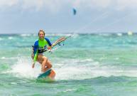 A woman kitesurfing smiles while she rides a wave onto shore